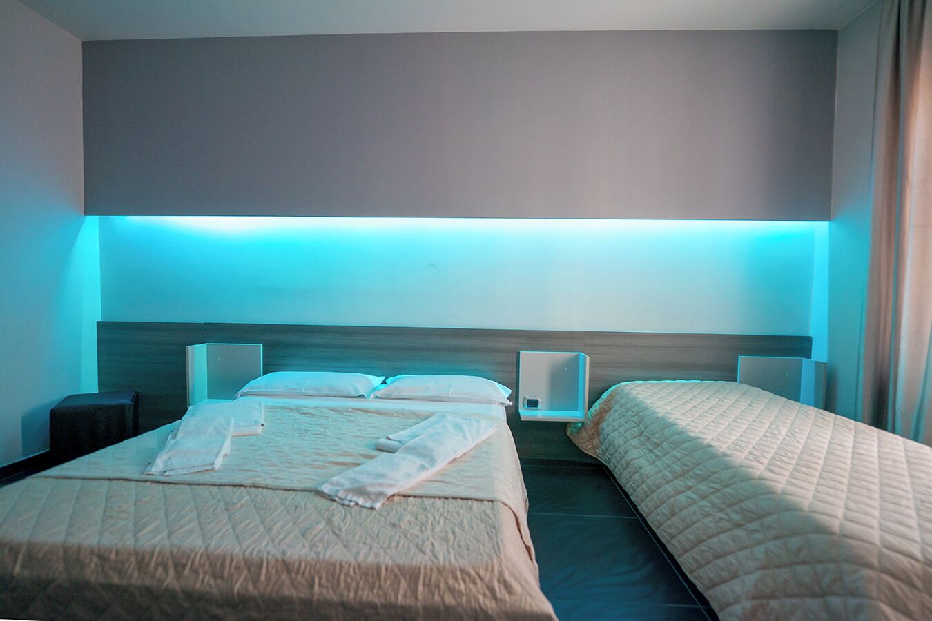 A hotel room with two beds, a nightstand, and a wall-mounted light fixture.