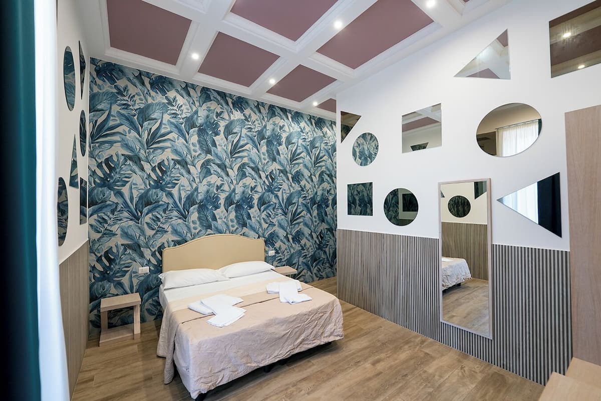 A bedroom with a bed, a nightstand, a mirror, and a wall with circular and rectangular mirrors.