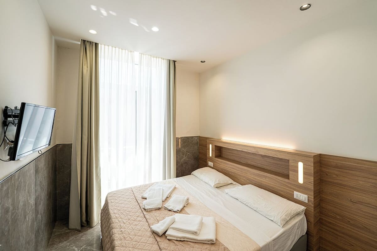 A hotel room with a bed, a TV, and a window with curtains.