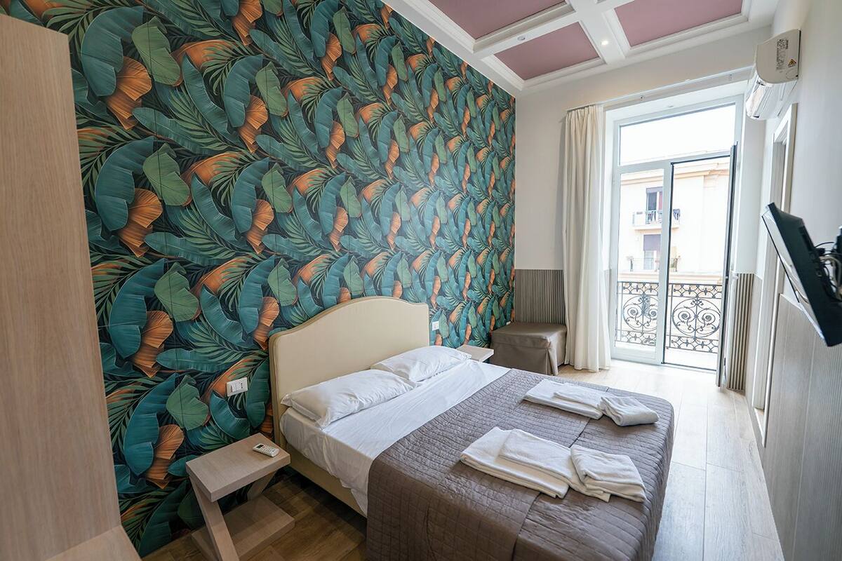 A bedroom with a bed, a bedside table, and a view of the outside balcony.