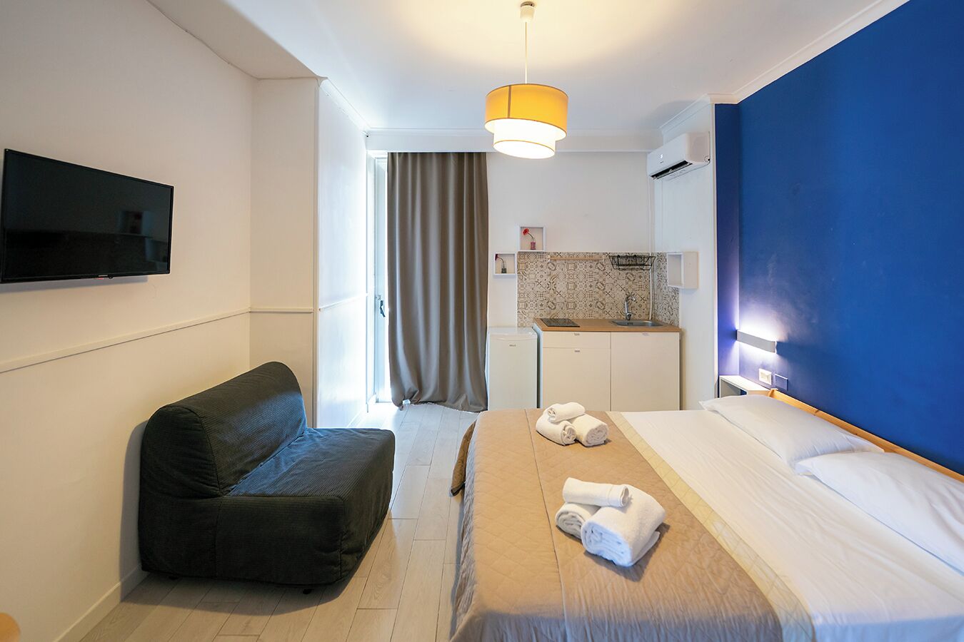Una camera d'albergo con un letto, un divano, una televisione, angolo cottura e bagno.