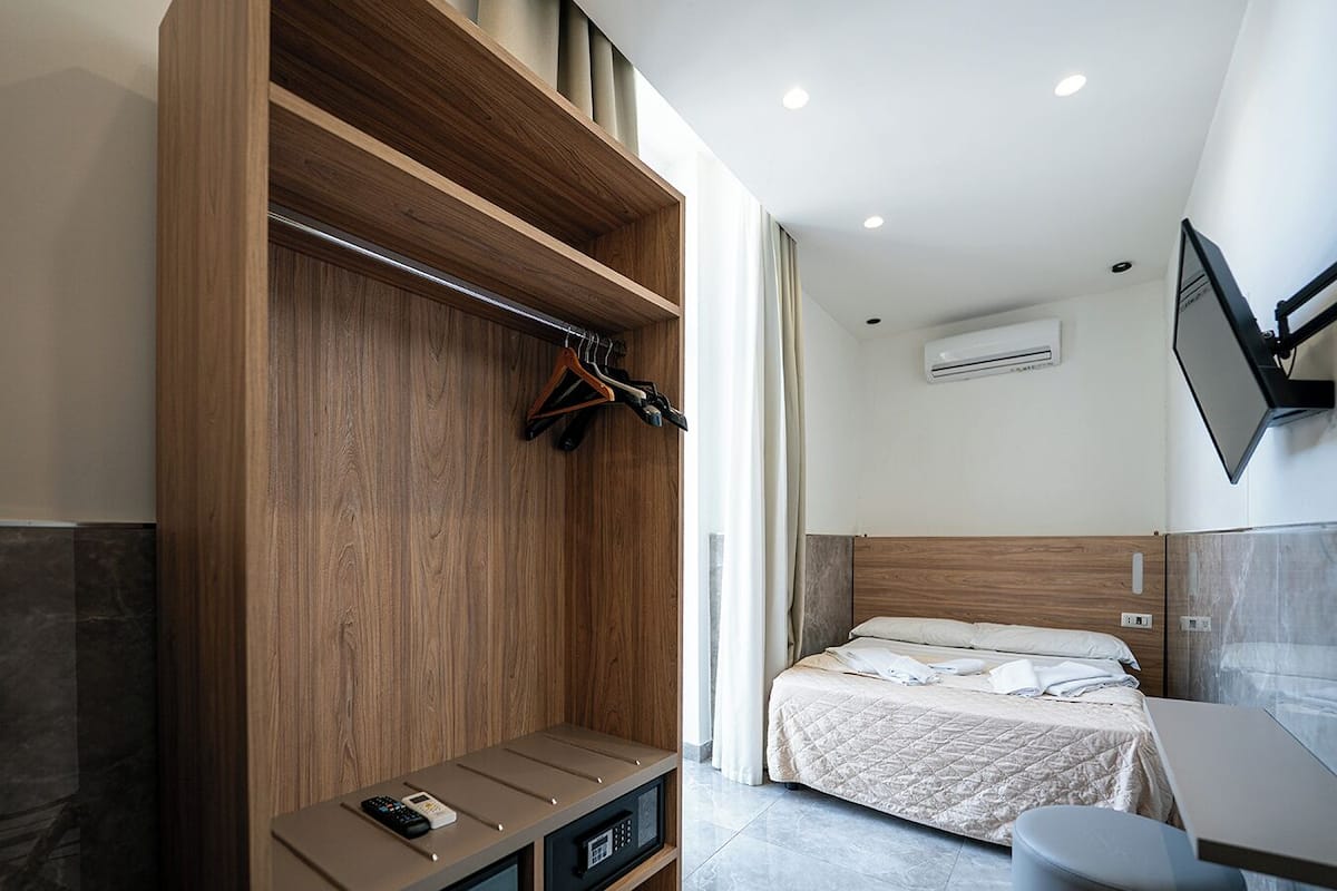 A modern hotel room with a bed, a desk, a wardrobe, and a TV mounted on the wall.
