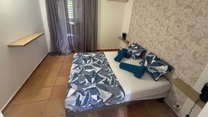 A bedroom with a bed, curtains, an air conditioning unit, a shelf, and a patterned wall. - Bungalow Korail (Pointe-Noire)