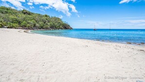 A beach with clear blue water, a sandy shore, and a small island with trees in the background. - Bungalow Korail (Pointe-Noire)