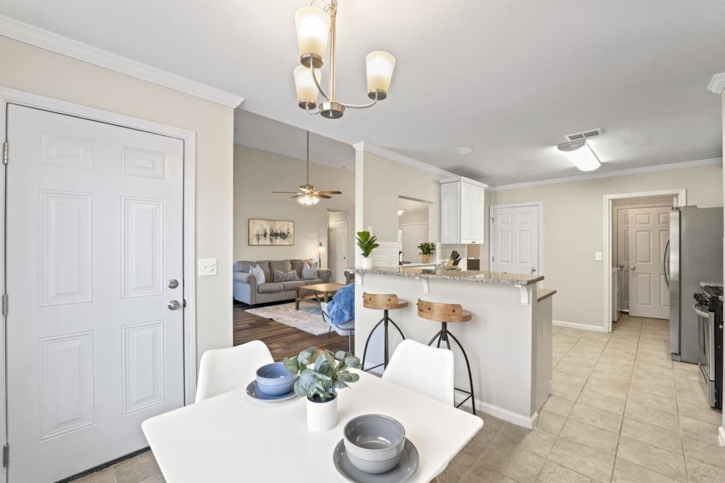 A modern kitchen with a central island, white cabinetry, and a dining area with a white table and chairs.