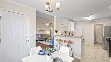 A modern kitchen with a central island, white cabinetry, and a dining area with a white table and chairs.