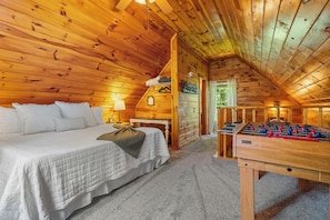 Ein Schlafzimmer einer Holzhütte mit einem Bett, einem Kicker und einem Fenster mit Blick auf Grün.