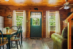 A wooden cabin interior with a dining table, chairs, a sofa, a television, and a door with a bear symbol. - Cabin with Hot Tub.15 min to Gatlinburg&Pigeon Forge. (Sevierville)