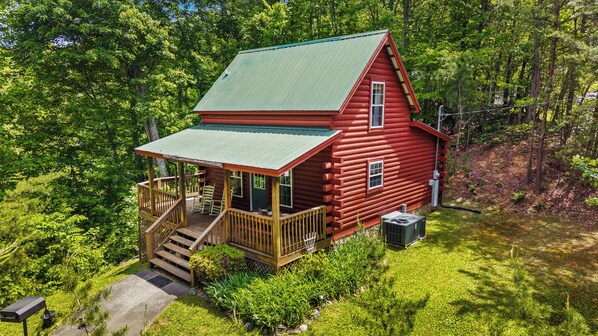 Eine rote Blockhütte mit grünem Dach, einer Veranda und einer kleinen Terrasse.