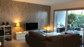 A modern living room with a flat-screen TV, a sofa, a coffee table, and a bookshelf. - Appartement 78 m² 1 chambre, terrasse et garage (Aix-les-Bains)