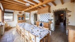 Une cuisine rustique avec des poutres en bois, une longue table à manger et une arche en pierre.