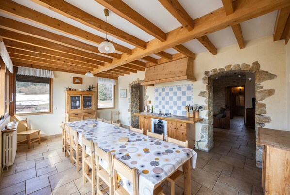 Una cocina rústica con vigas de madera, una larga mesa de comedor y un arco de piedra.