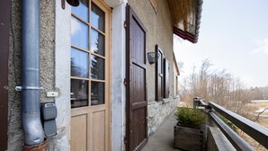 Un bâtiment en pierre avec des portes et des fenêtres en bois, un tuyau en métal et un petit pot de fleurs sur le porche.