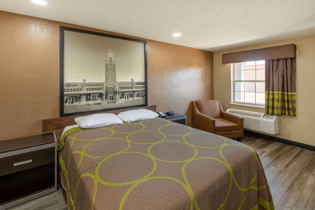 A hotel room with a bed, a chair, a desk, and a large framed picture on the wall.