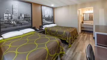 A hotel room with two beds, a large window with cityscape views, a bathroom with a mirror and sink, and a desk with a chair.