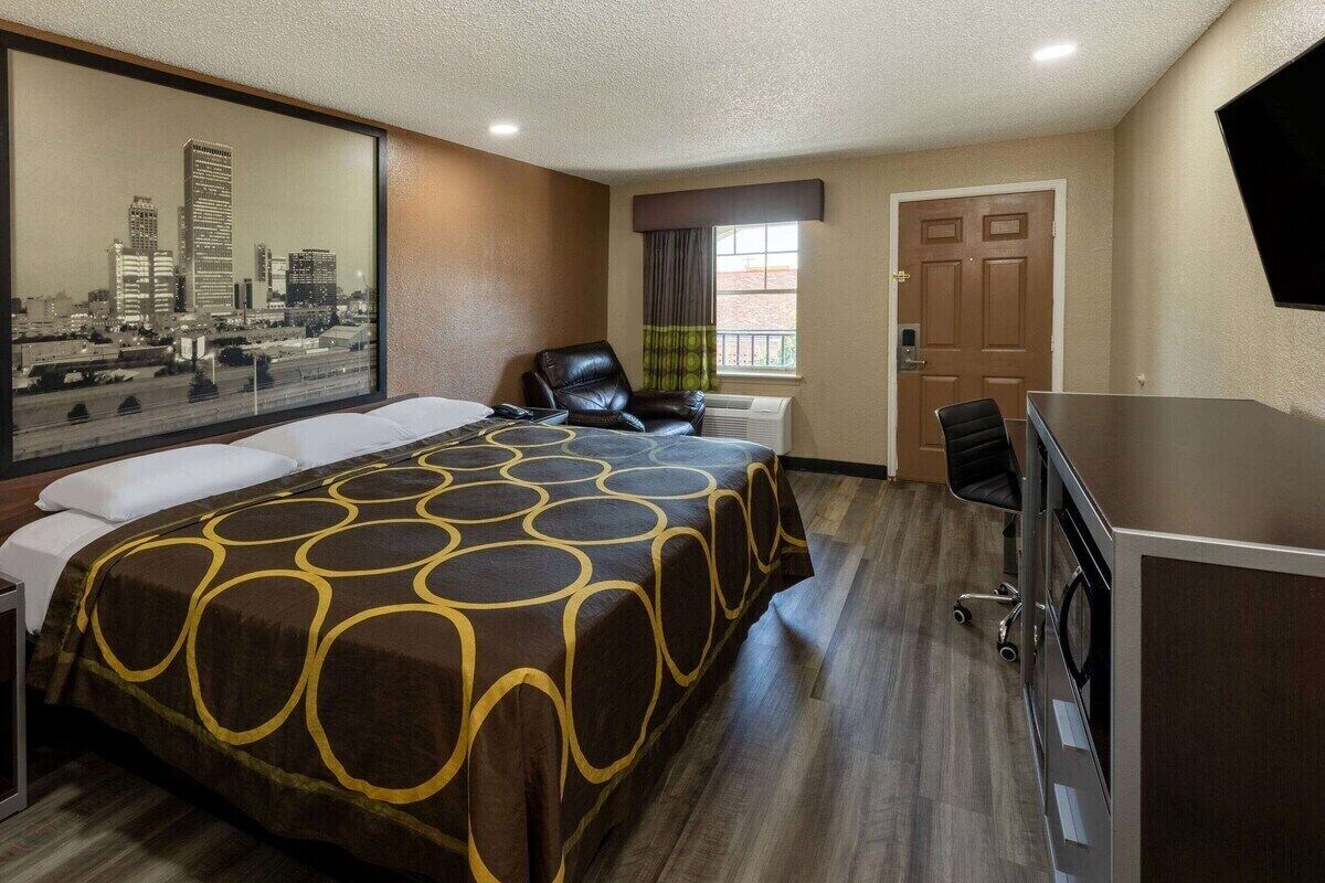 A hotel room with a large bed, a desk, a chair, and a cityscape view.