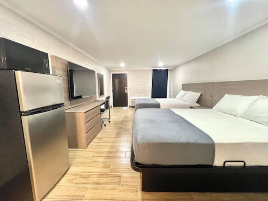 A modern hotel room with a bed, a desk, a television, and a refrigerator.