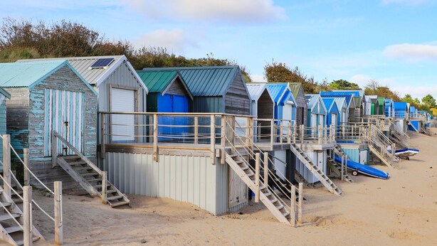 A row of beach huts with wooden stairs leading up to each one. - Angorfa Apartment (Pwllheli)