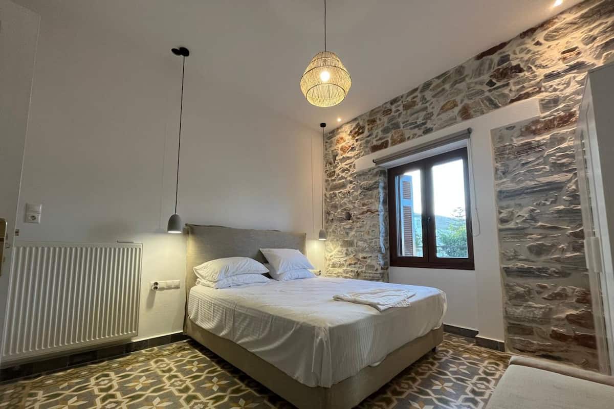 Ein Schlafzimmer mit einer Steinsandsteinwand, einem Bett mit weißer Bettwäsche, einem gemusterten Boden und einer hängenden Leuchte.