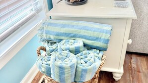 Una habitació amb una cistella de vimet plena de tovalloles enrotlades, una taula auxiliar blanca amb un objecte decoratiu i una paret blava.