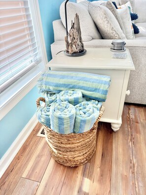 Ein Zimmer mit einem Korbwäscheschrank, gefüllt mit gerollten Handtüchern, einem weißen Beistelltisch mit einem dekorativen Gegenstand und einer blauen Wand.