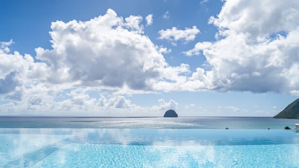 Un ciel d’un bleu limpide parsemé de nuages, une mer calme et une île lointaine.