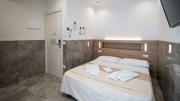Een hotelkamer met een bed, een deur, een bedieningspaneel aan de muur en een flatscreen televisie.