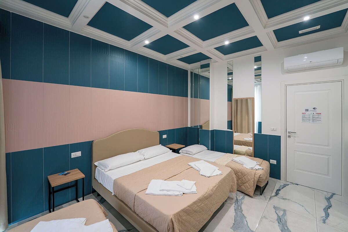 Een hotelkamer met twee bedden, een klein nachtkastje, een spiegel en een deur met een bordje.