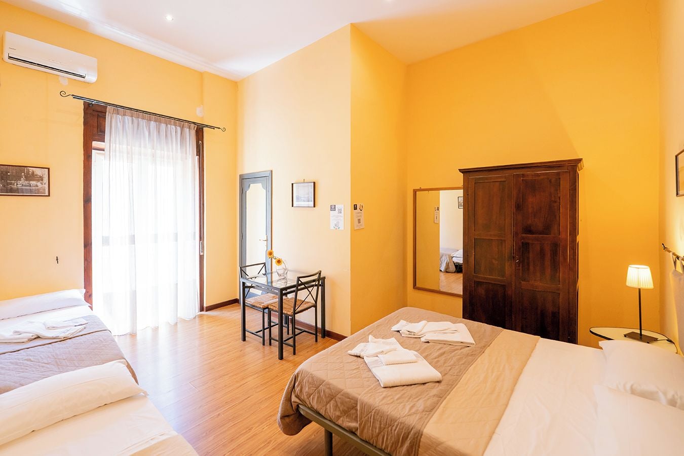 A hotel room with two beds, a desk with a chair, a mirror, and a wardrobe.