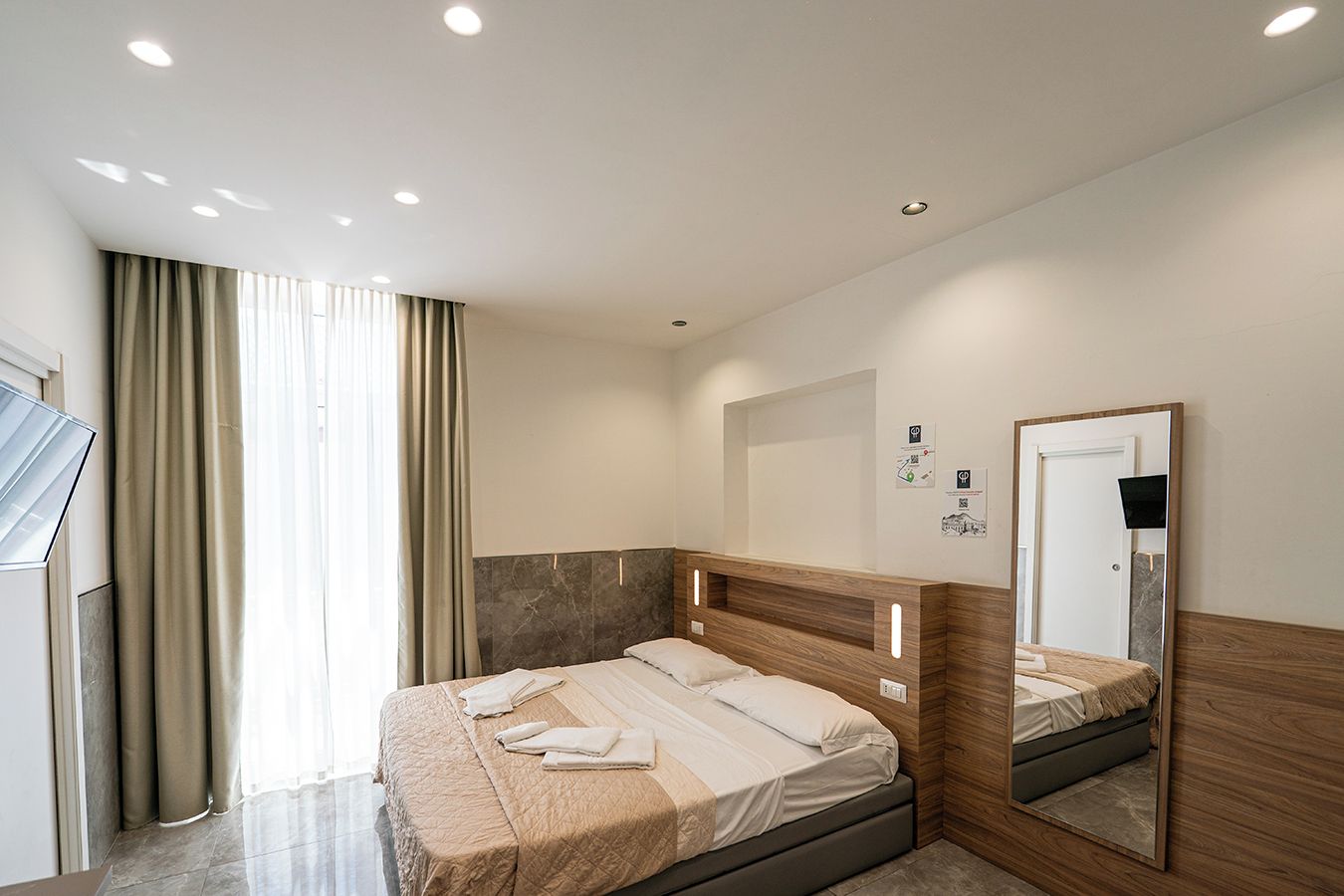 Ein modernes Hotelzimmer mit einem großen Bett, einem Spiegel und einem Fenster mit Vorhängen.