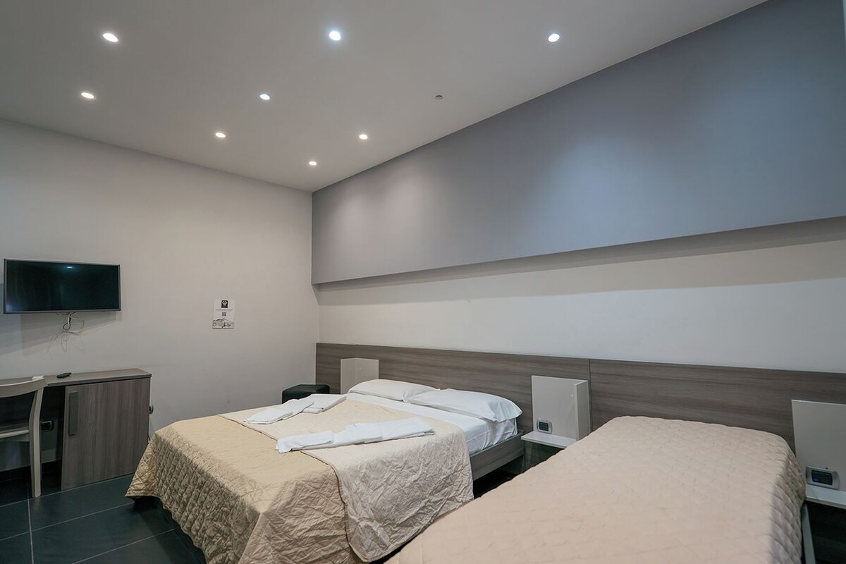 Une chambre d’hôtel avec deux lits, un bureau, une télévision et un climatiseur fixé au mur.