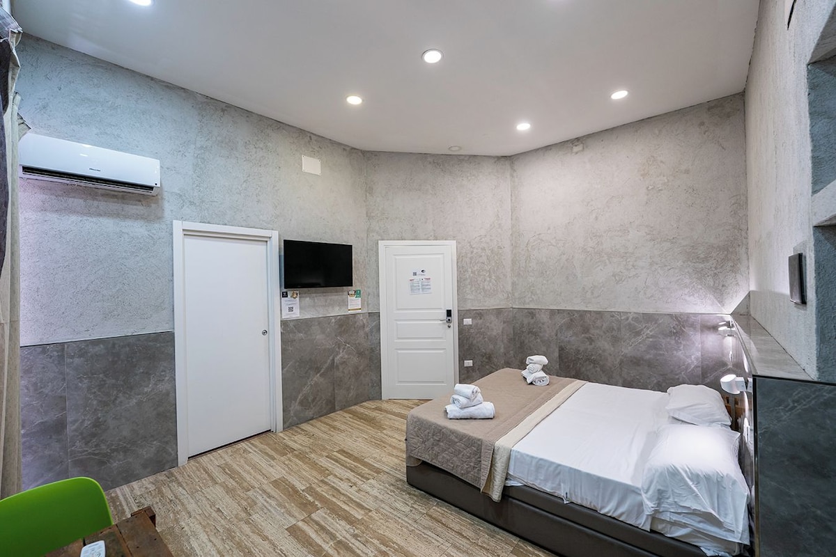 A modern hotel room with a bed, a TV mounted on the wall, and an air conditioning unit.