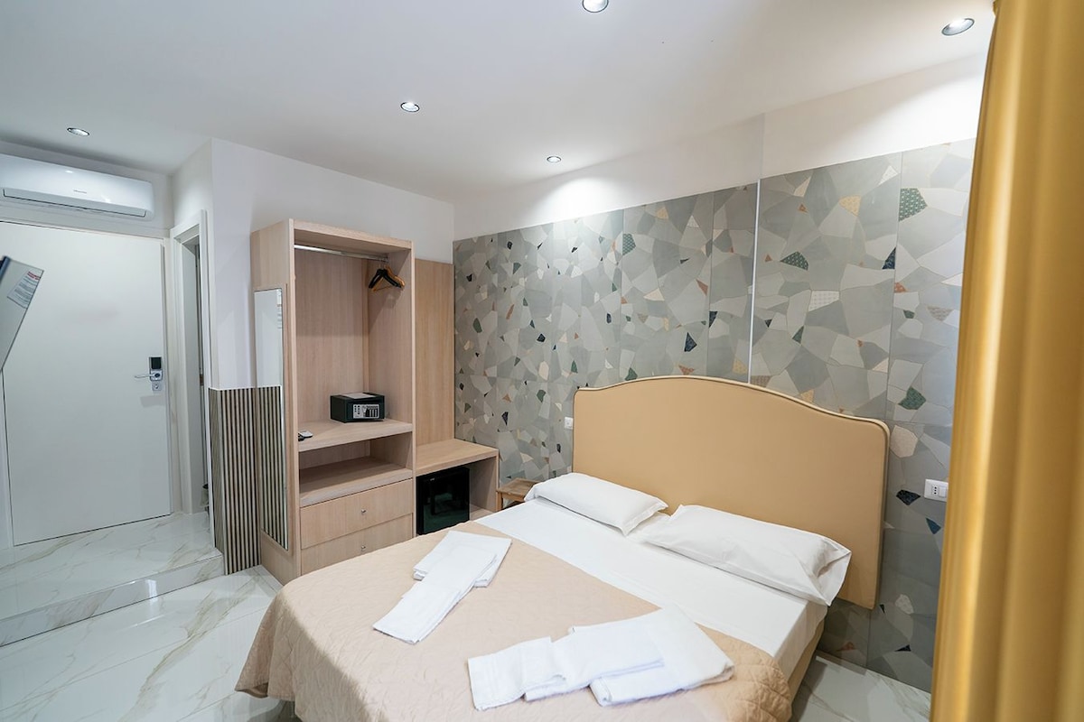 Ein modernes Hotelzimmer mit Bett, Kleiderschrank, Schreibtisch und einer Duschkabine.
