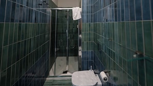 Une salle de bain avec des murs recouverts de carreaux verts, une douche en verre, des toilettes blanches et une serviette accrochée à la porte de la douche.