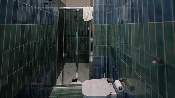 A bathroom with green-tiled walls, a glass shower enclosure, a white toilet, and a towel hanging on the shower door. - GREROS DANTE H. by Clapa Group dislocated hospitality (Naples)
