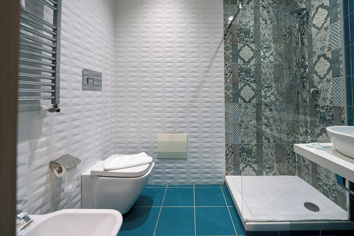 Un bagno con il water bianco, un bidet e una zona doccia con piastrelle decorate.