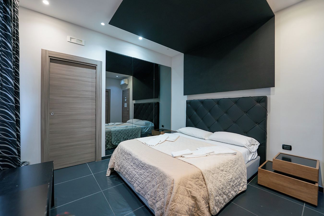 A modern bedroom with a large bed, a wardrobe, and a mirror.