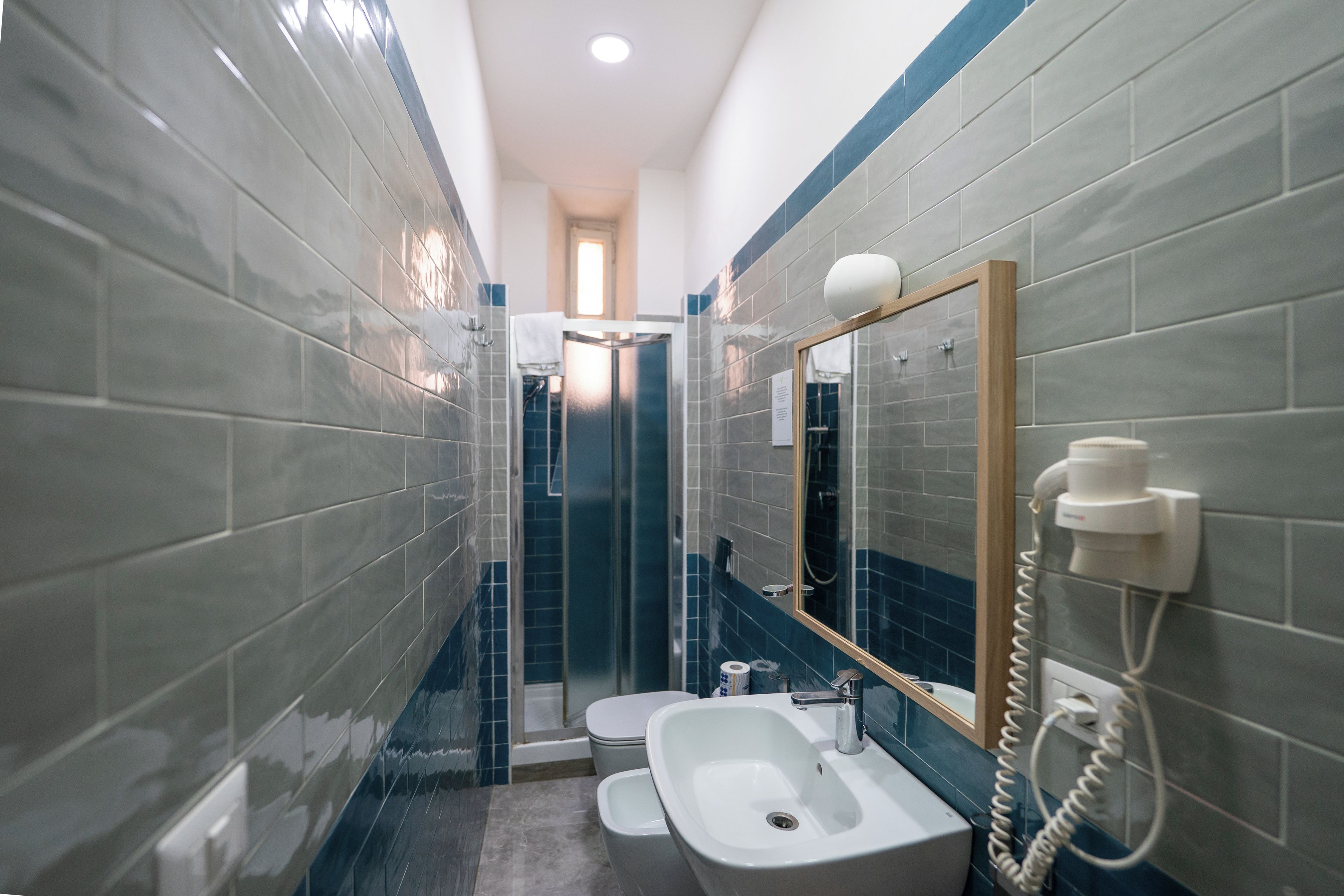 A narrow bathroom with a sink, mirror, and a telephone.
