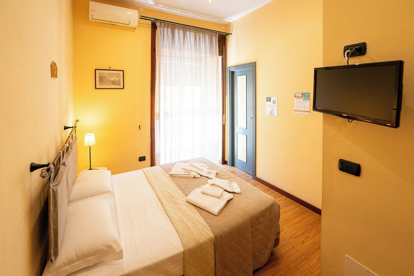 A hotel room with a bed, a TV, a lamp, and a window with curtains.