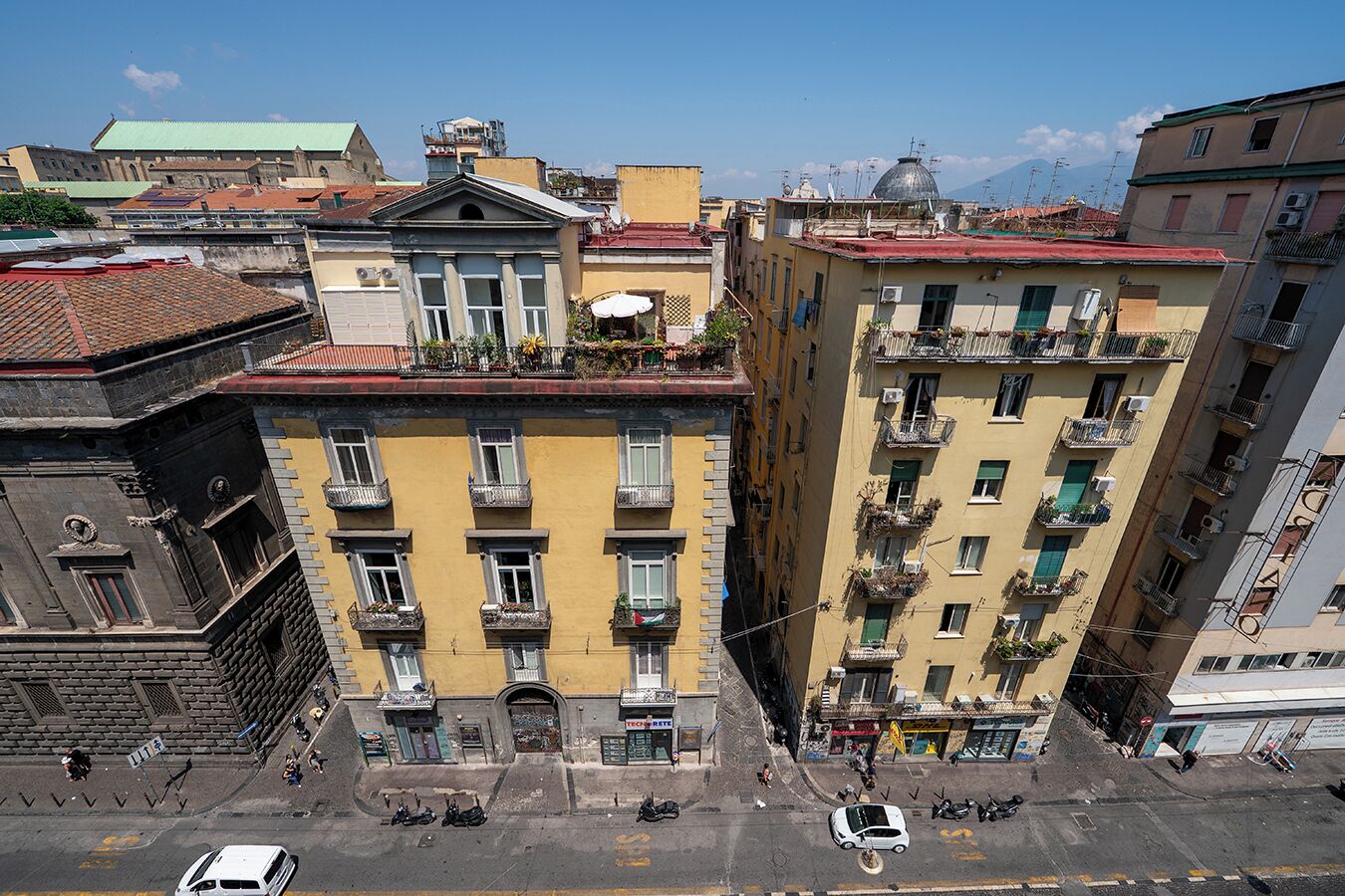 Una vista di strada in città, con edifici, tra cui un palazzo giallo con balconi e un'auto bianca parcheggiata.