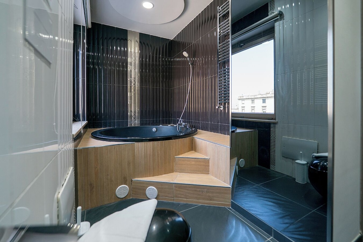 A modern bathroom with a freestanding bathtub, wooden steps, and a window providing a view of the city.