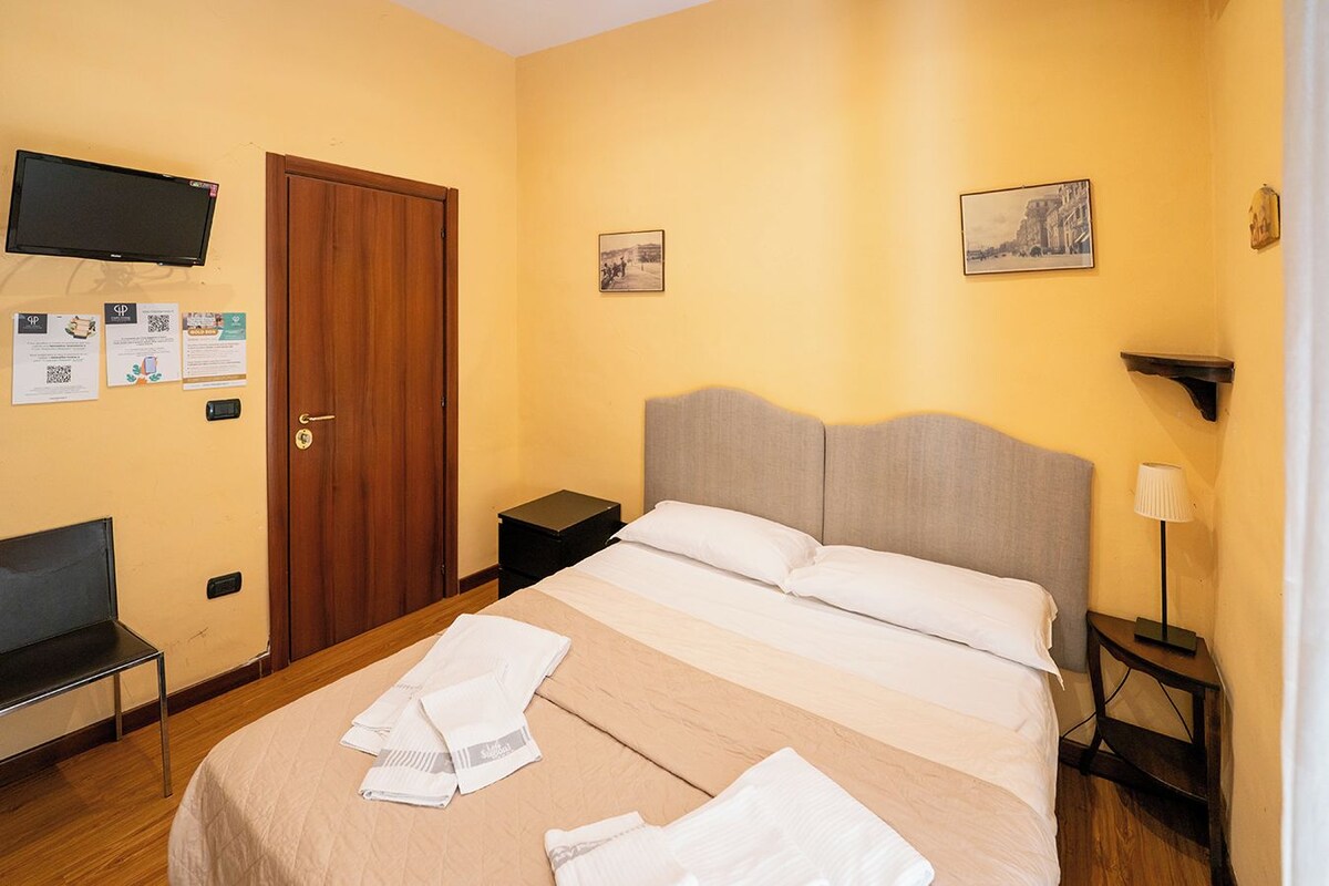 A hotel room with a bed, a desk, a chair, a TV, and a door.