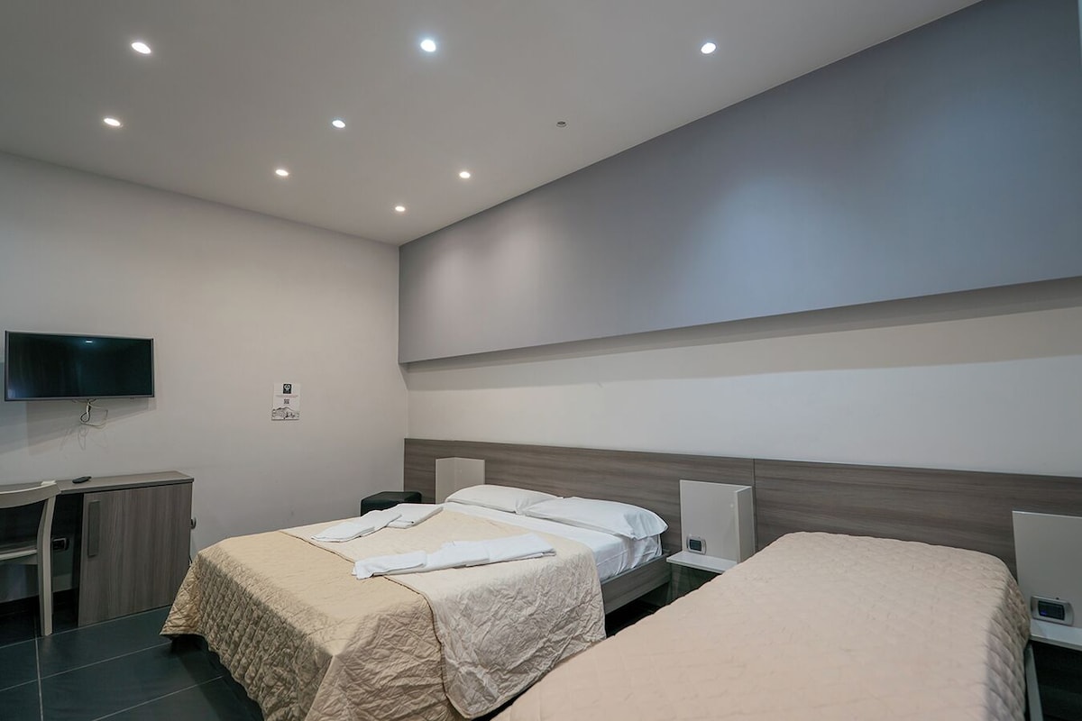 A hotel room with two beds, a desk, a TV, and a wall-mounted air conditioning unit.