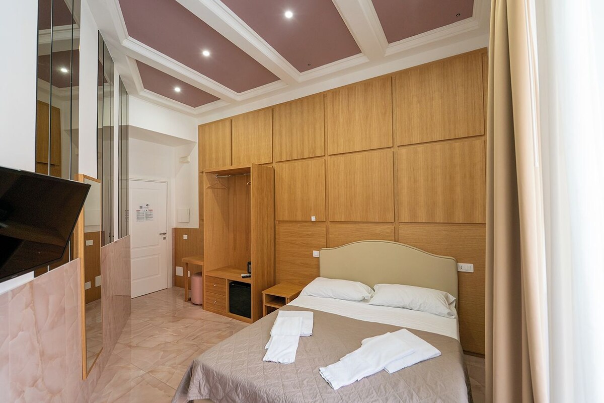 Een slaapkamer met een bed, een houten garderobe, een klein nachtkastje en een spiegel.