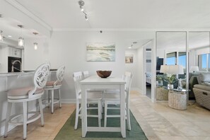 A dining area with a white table and chairs, a green rug, and a painting of a boat on the wall. - Waterfront Isla del Sol Condo w Balcony & Pool (St Petersburg)