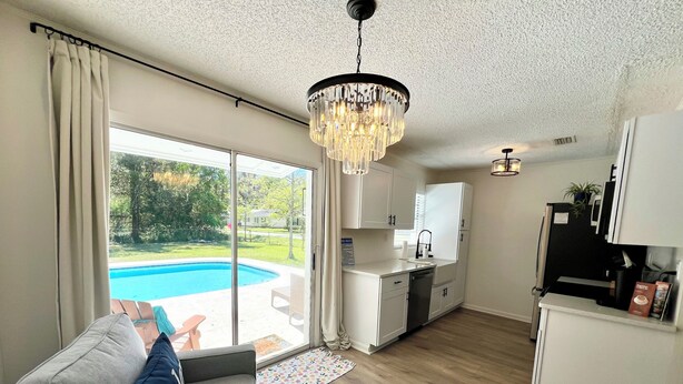 A modern living room with a grey sofa, a chandelier, and a view of a swimming pool. - Pool home • Near St. Augustine & Beaches (Hastings)