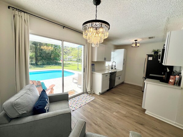 Ein modernes Wohnzimmer mit einem grauen Sofa, einer Chandelüster und Blick auf einen Swimmingpool.