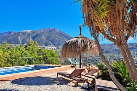 Un espace piscine avec des chaises longues, un parasol en chaume et une vue sur la montagne.. Maison de campagne 'La Perla Andaluza' avec vue sur la montagne, Wi-Fi et climatisation