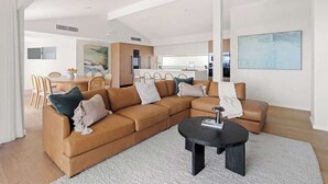 En moderne stue med en hjørnesofa, et rundt sofabord og et spiseområde i baggrunden.