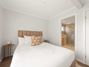 Un dormitorio con una cama grande, cabecera de madera, una mesita de noche con lámpara y un baño visible a través de una puerta abierta.